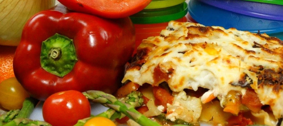 A fresh-baked vegetable lasagna surrounded by colorful peppers and tomatoes
